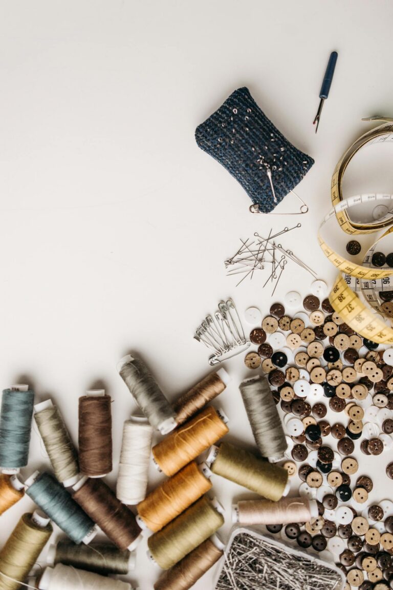 Artistic flat lay of sewing essentials including threads, buttons, and pins on a white surface.