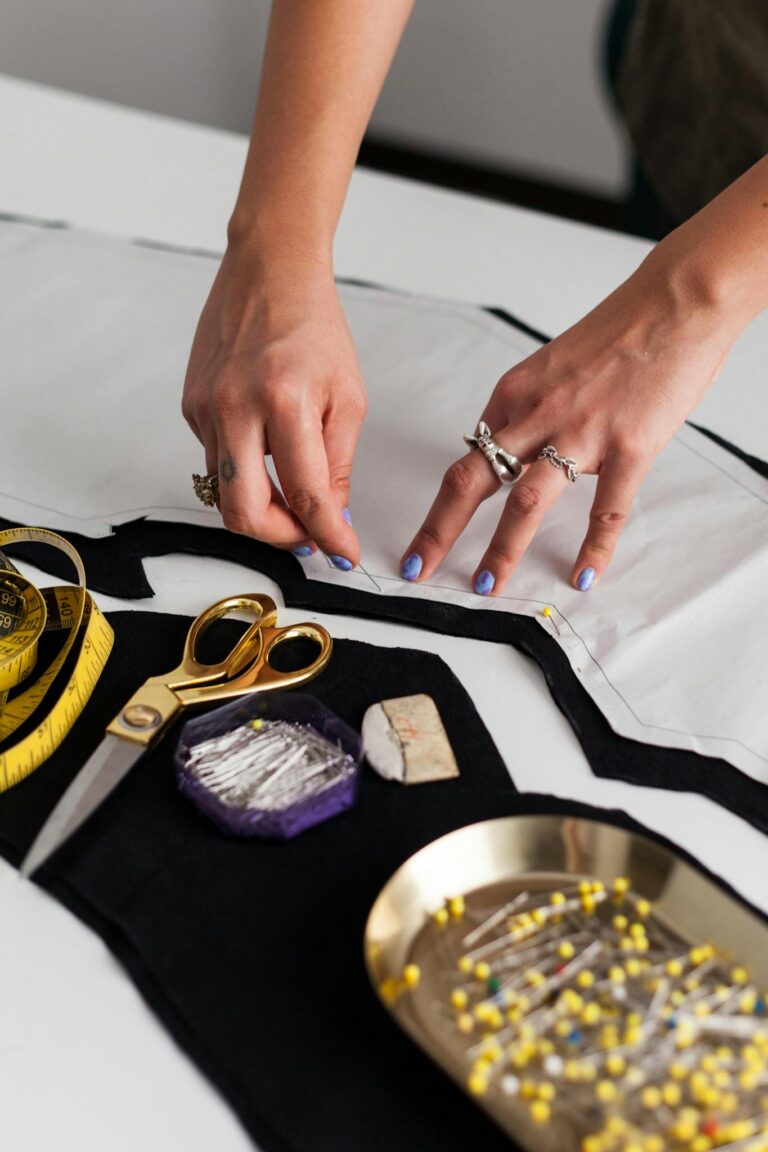 Hands working on fabric with sewing tools in a fashion designer's workspace.