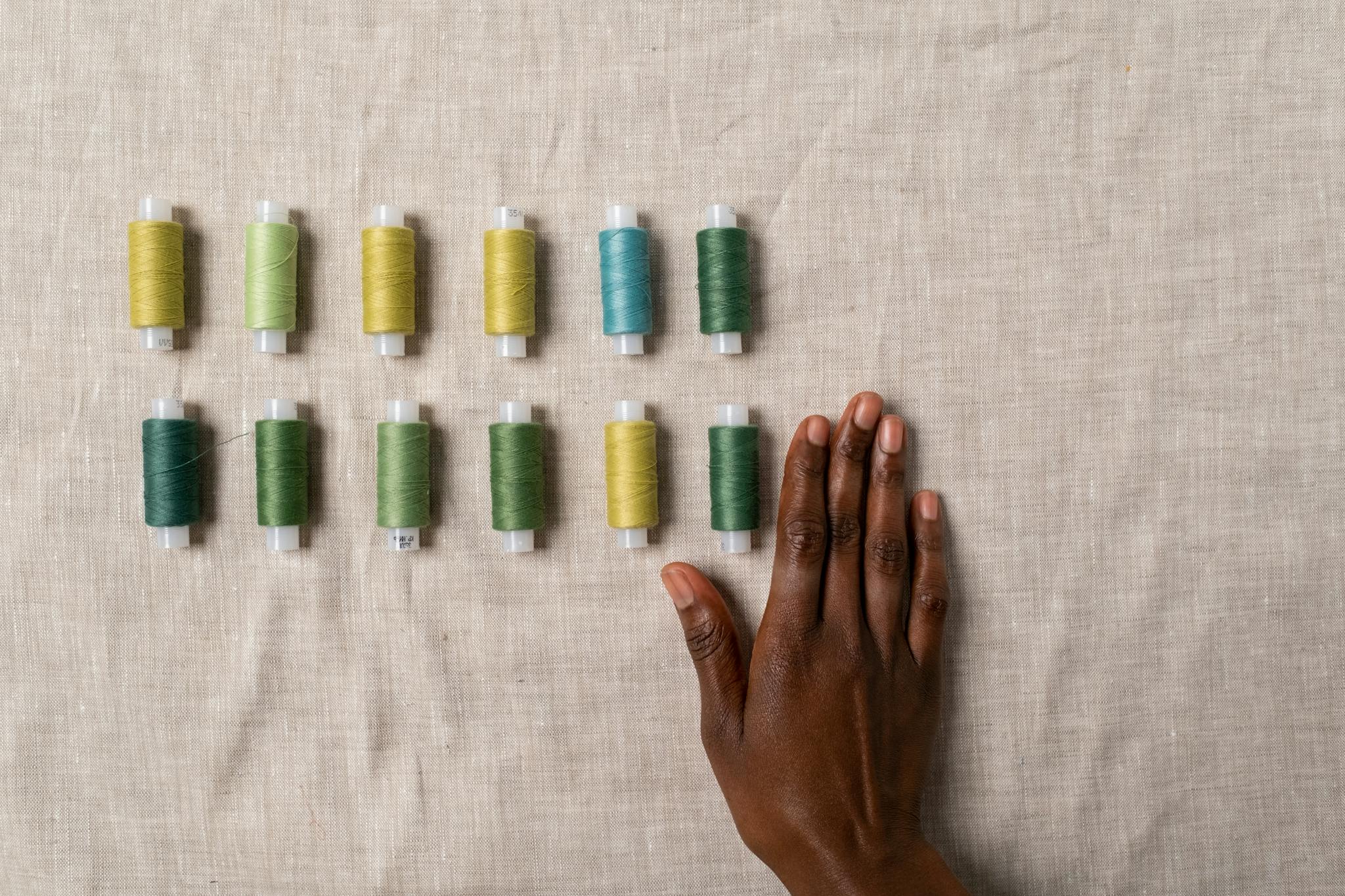 Top view of colorful sewing threads with a hand on fabric, ideal for crafting and design themes.